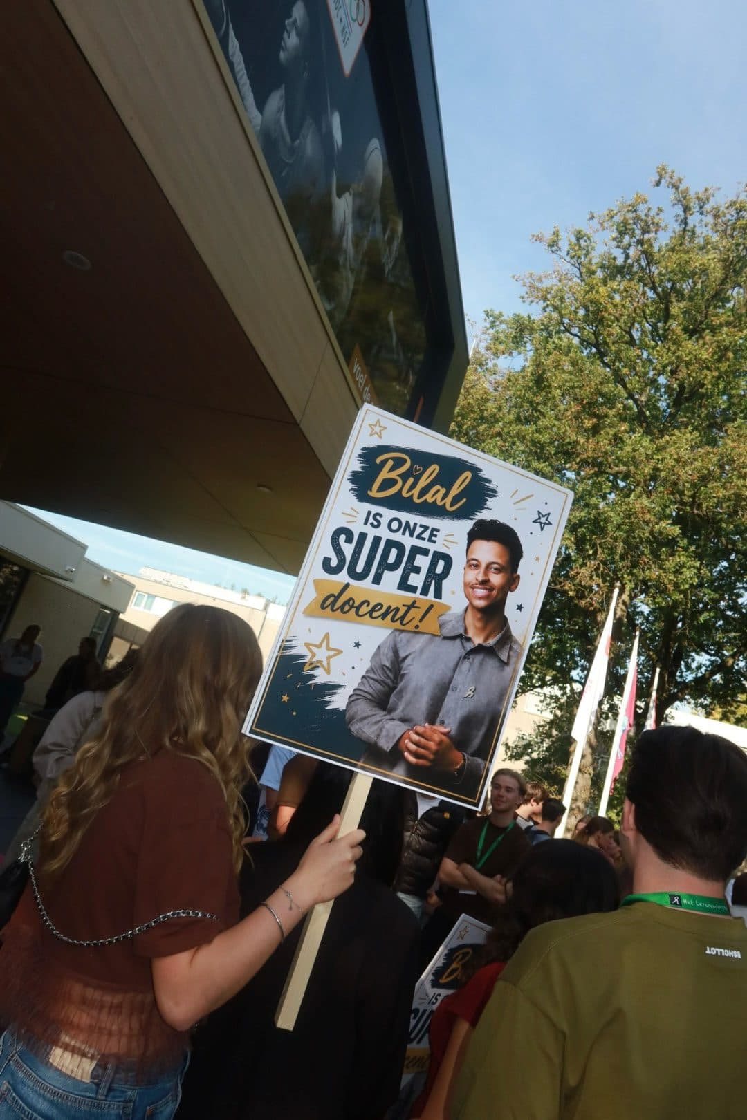 Een leerling houdt een bord omhoog met de tekst 'Bilal is onze super docent!'