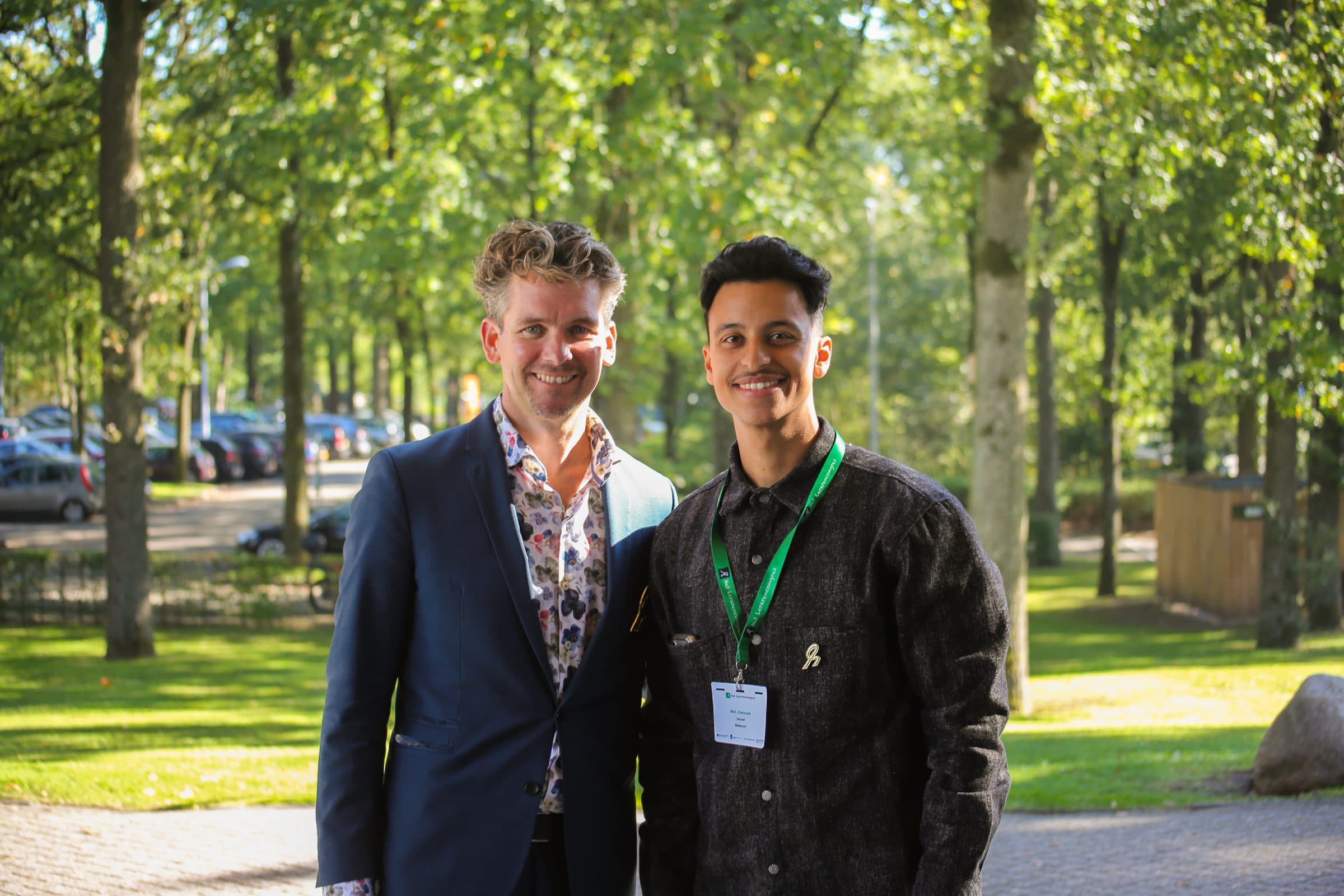 Bilal staat buiten tussen de bomen naast de presentator van het congres