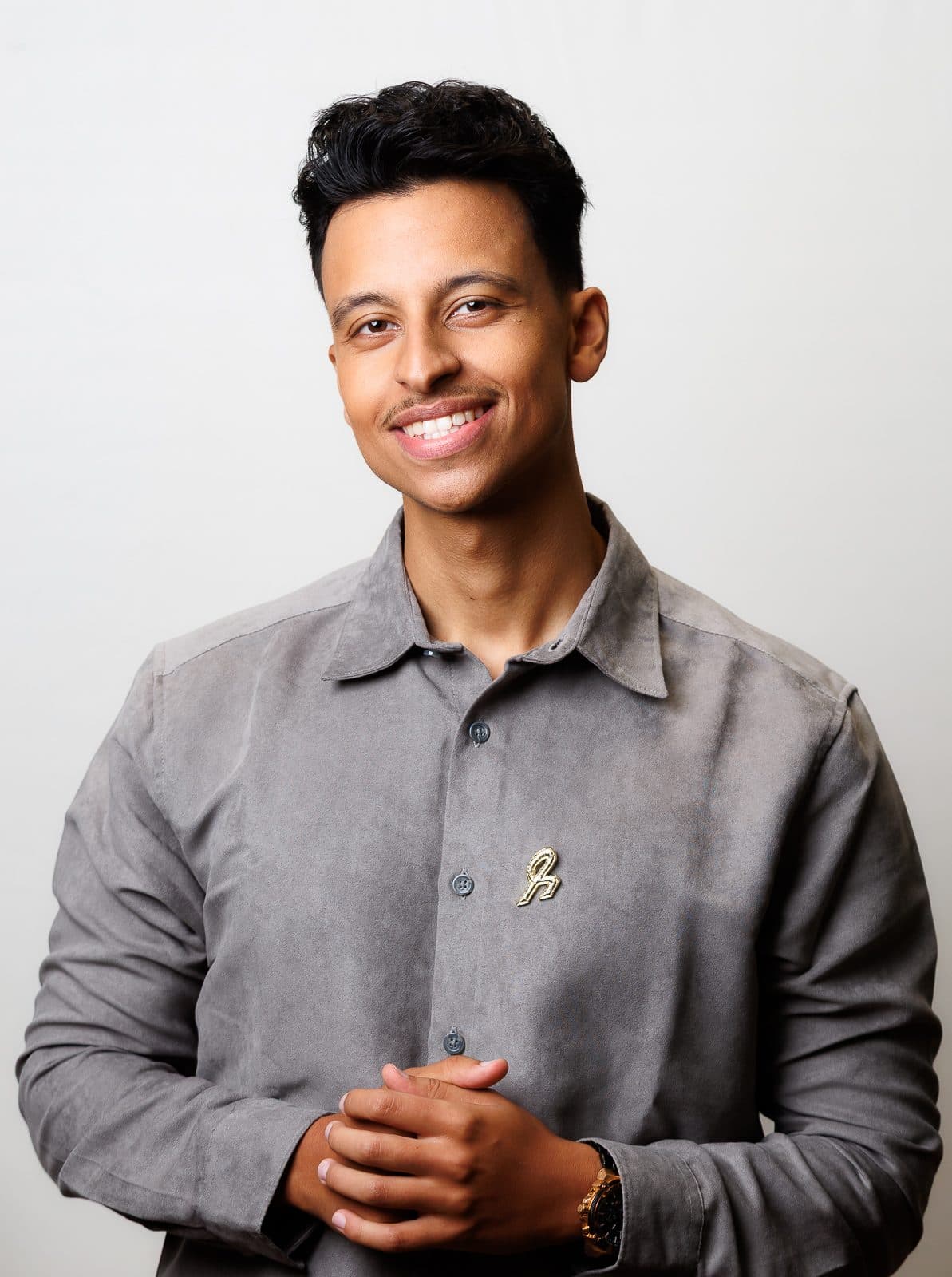 Portret van Bilal Chetouani in een grijs overhemd, glimlachend met gevouwen handen tegen een lichte achtergrond