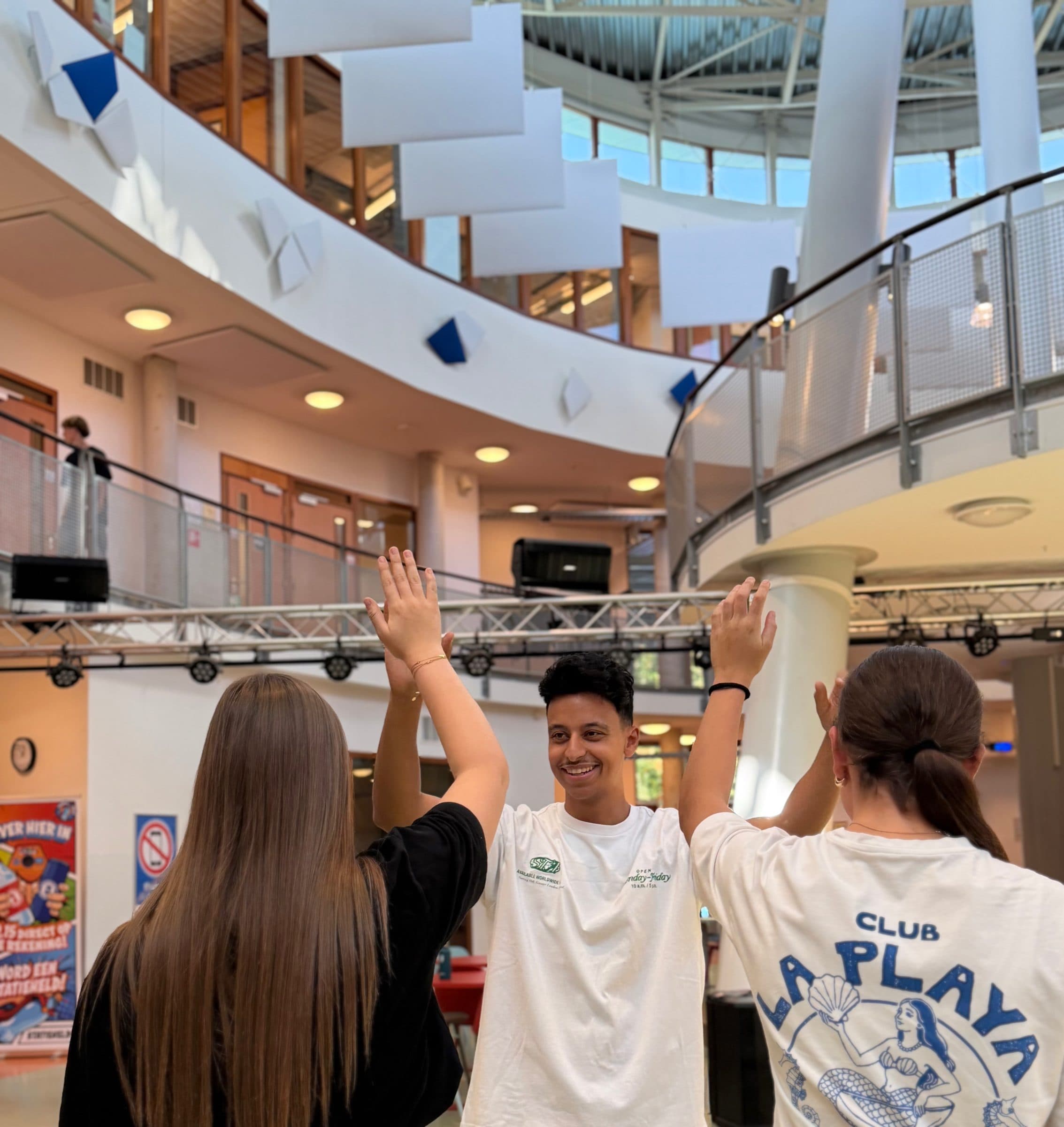 Bilal geeft twee leerlingen een high five in het atrium van school